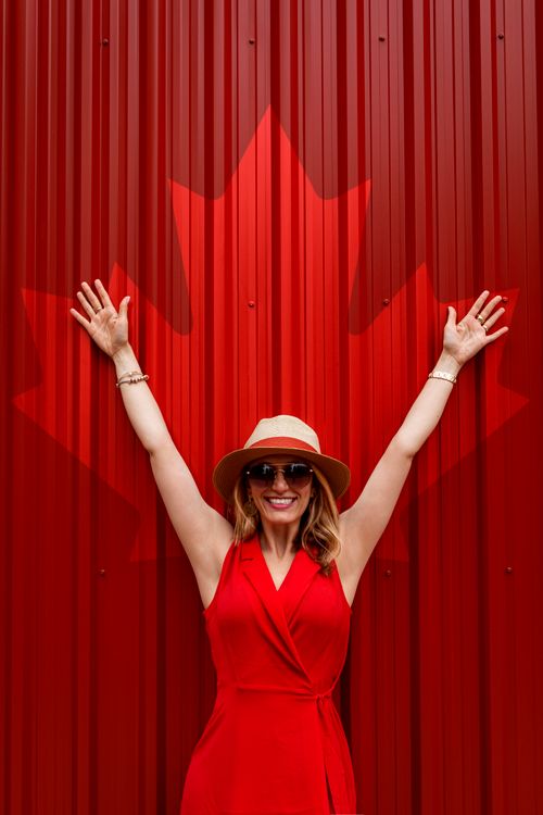 Free Smiling woman in red dress and hat, arms raised against a maple leaf background in Toronto. Stock Photo