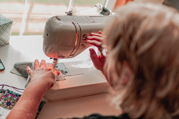 Hands binding the edge of a mini quilt with coordinated fabric, quilting and binding class online