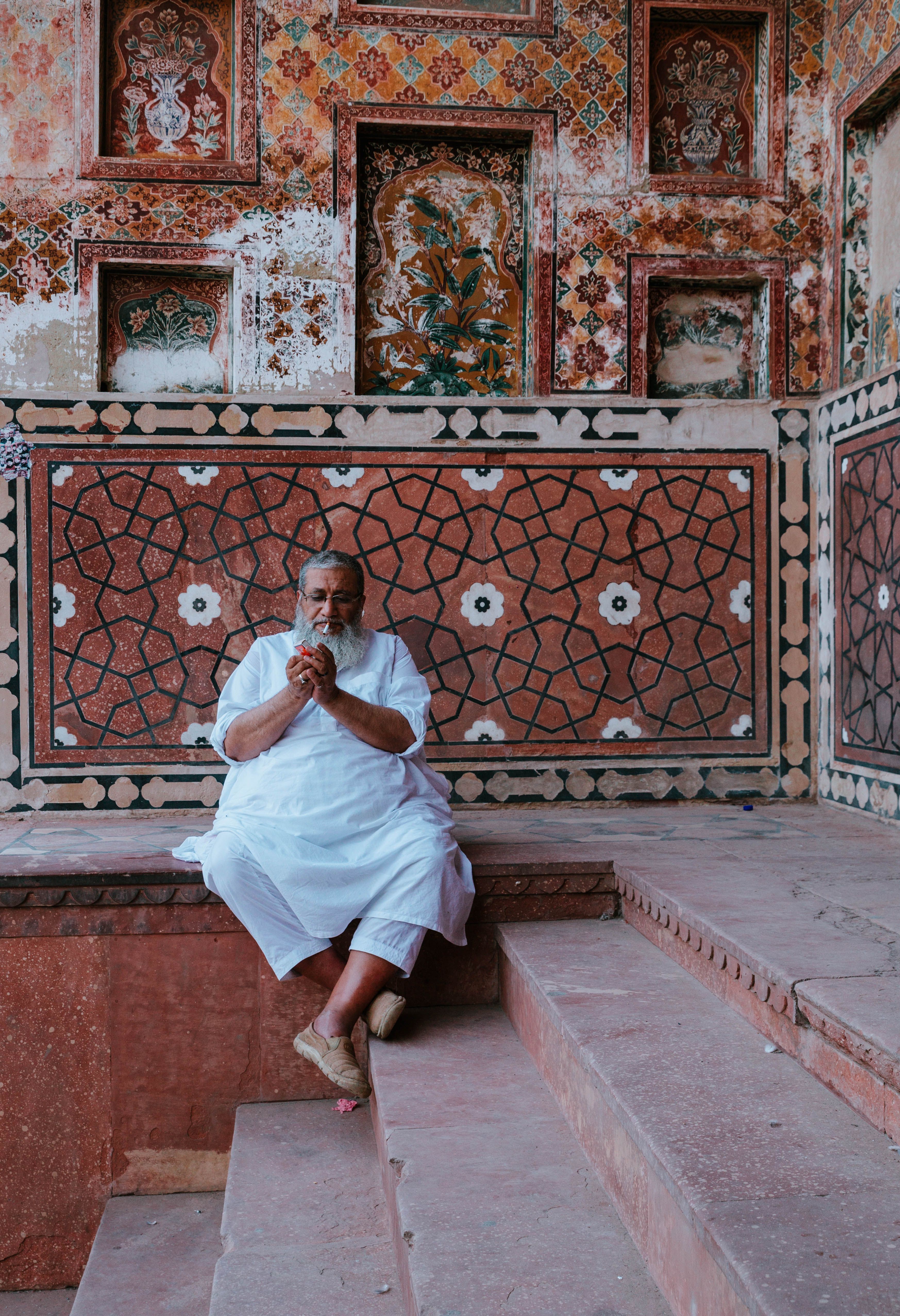Elderly man meditating in front of detailed mosaic tiles at Wazir Khan Mosque, Lahore.