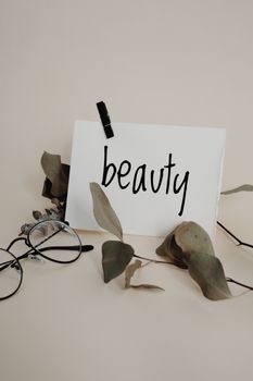 Elegant still life with eyeglasses, eucalyptus leaves, and 'beauty' note.
