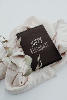 A chic flat lay of a Happy Birthday card on a linen cloth with decorative leaves.