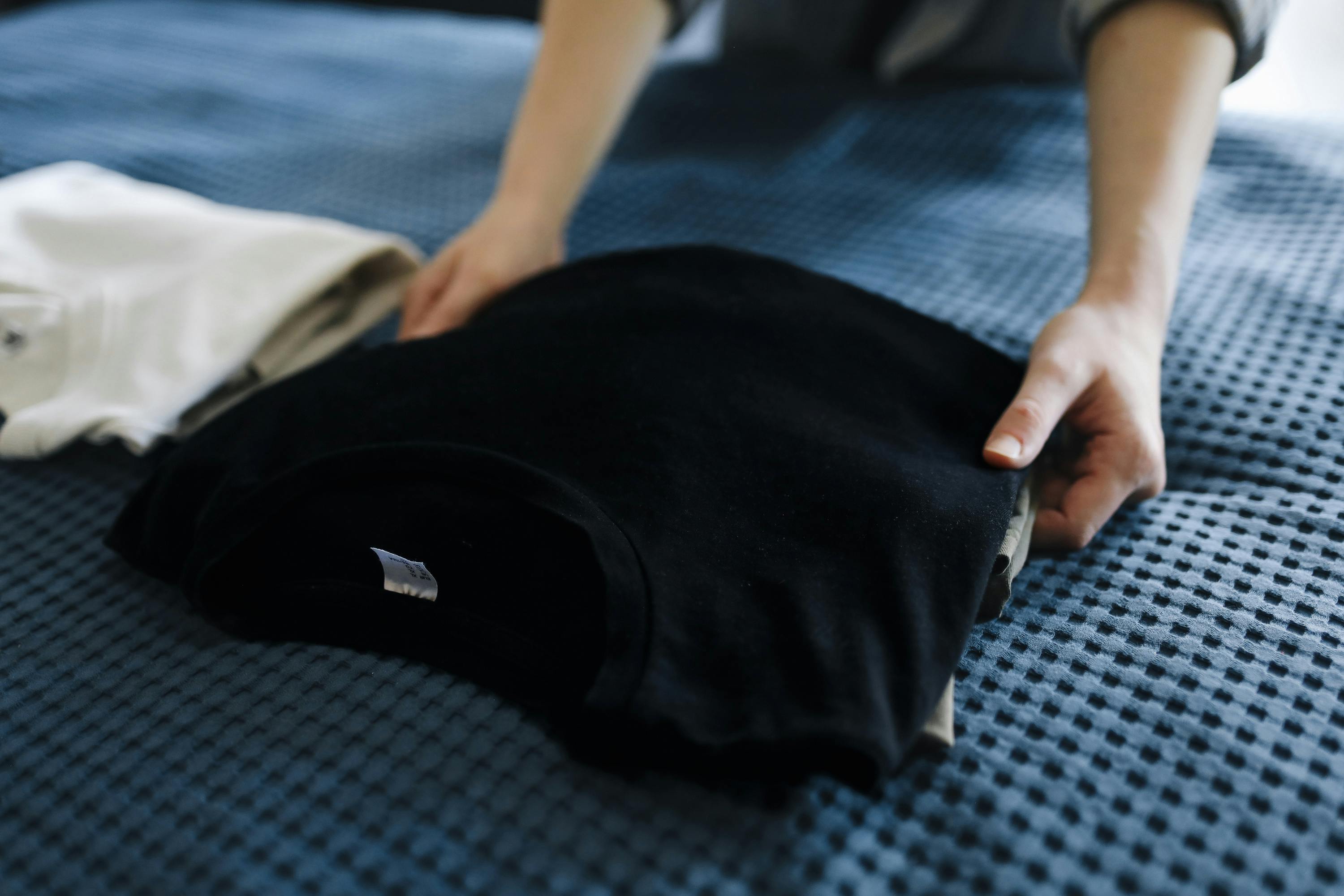 Free Close-up of a person folding T-shirts on a bed, showcasing neat housekeeping. Stock Photo