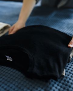 Close-up of a person folding T-shirts on a bed, showcasing neat housekeeping.