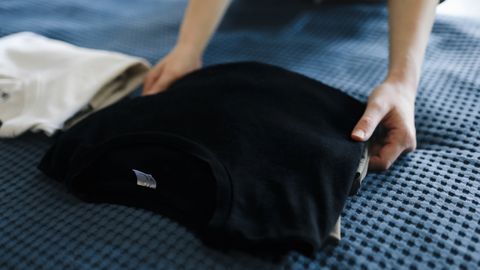 Close-up of a person folding T-shirts on a bed, showcasing neat housekeeping.