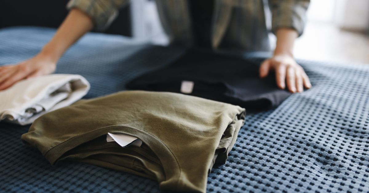 Como dobrar roupas Marie Kondo Mãos dobrando camisetas sobre a cama
