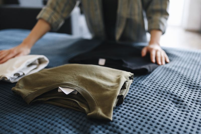 Hands folding clean t-shirts into a neat stack on a bed