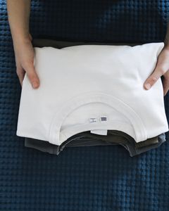 Hands folding a white shirt on a blue textured bedspread, focusing on organizing clothes.