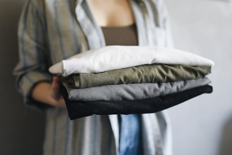 A Person Holding A Stack Of Neatly Folded Shirts