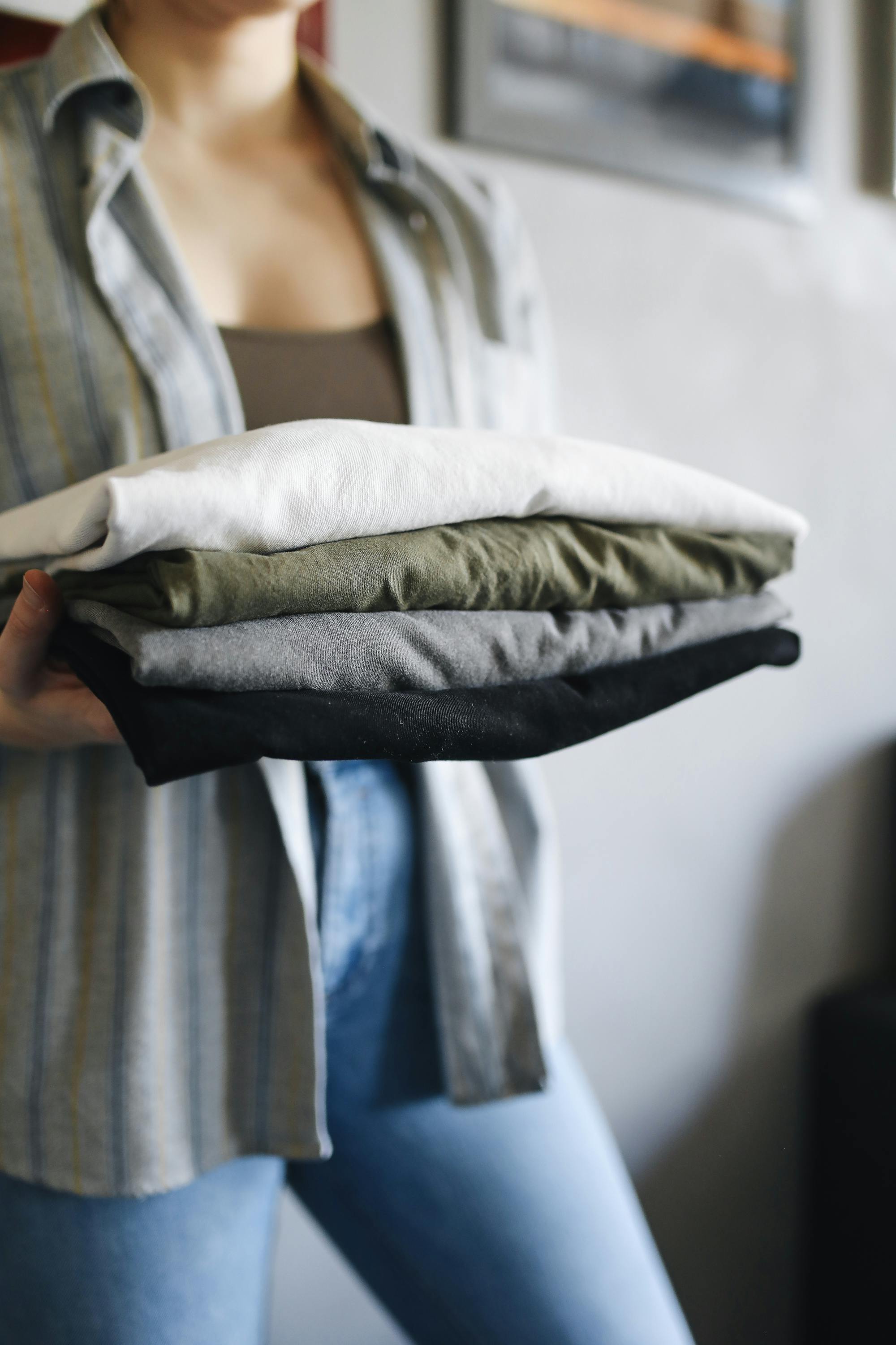 Free A person holding a stack of neatly folded shirts indoors, emphasizing organization and chores. Stock Photo