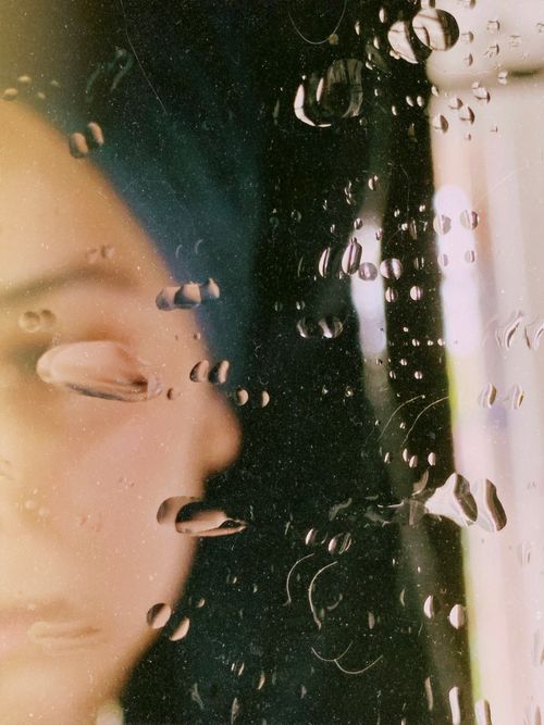 Free Soft focus portrait of a person behind a rain-covered window creating a moody and introspective atmosphere. Stock Photo