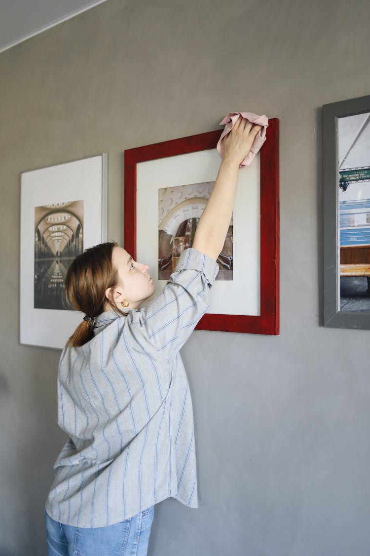 A Woman Cleaning The Display Frames On The Wall