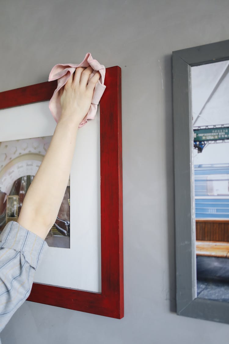 A Person Wiping A Picture Frame Hanging On The Wall