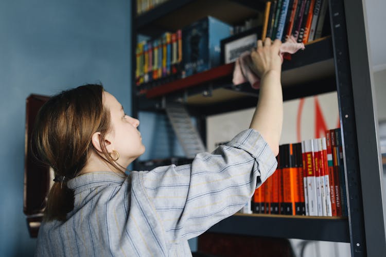 A Woman Wiping A Bookshelf With A Cloth