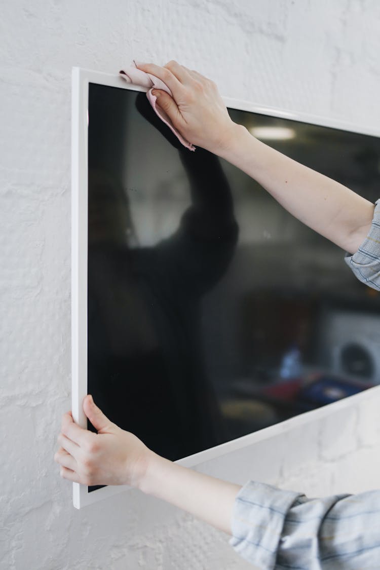 A Person Wiping A Television Mounted On Wall With A Cloth