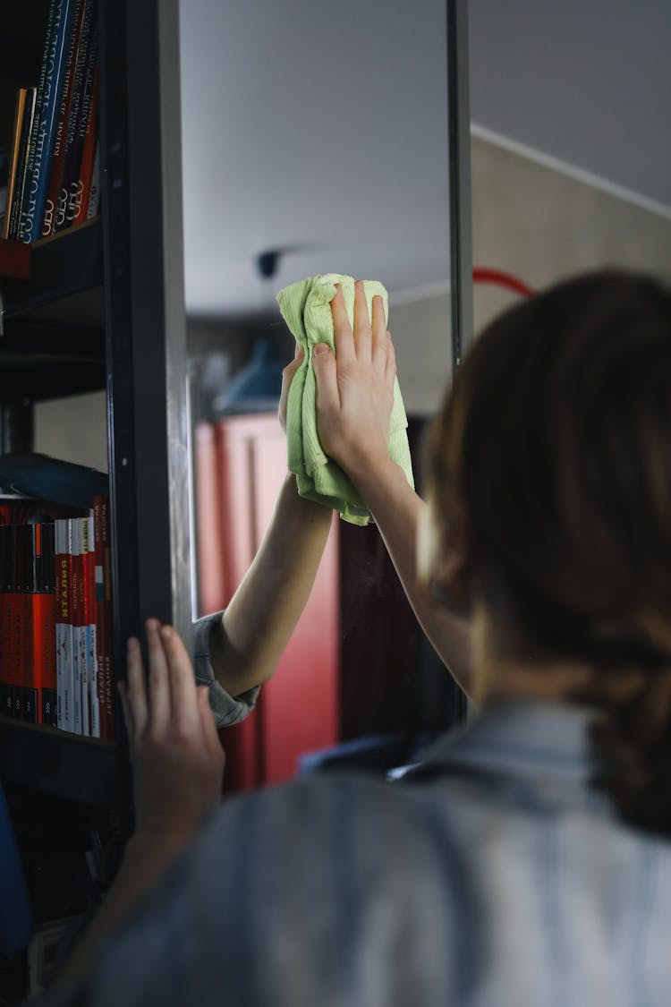 A Person Wiping A Mirror With A Green Cloth