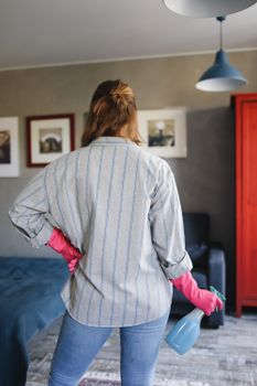 一位成年妇女戴着手套、拿着喷雾瓶，准备在室内进行清洁