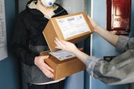 A Person Handing Out Cardboard Boxes to a Person Wearing a Face Mask