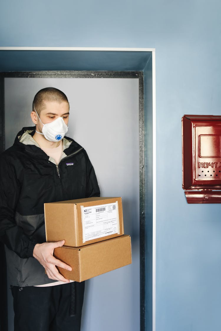 A Man Wearing Facemask Holding Cardboard Boxes