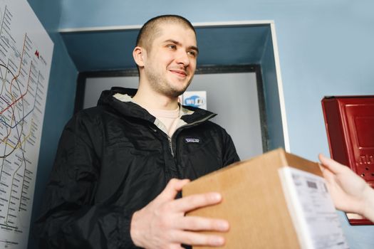 Smiling delivery person hands over a cardboard box indoors, conveying a friendly service.