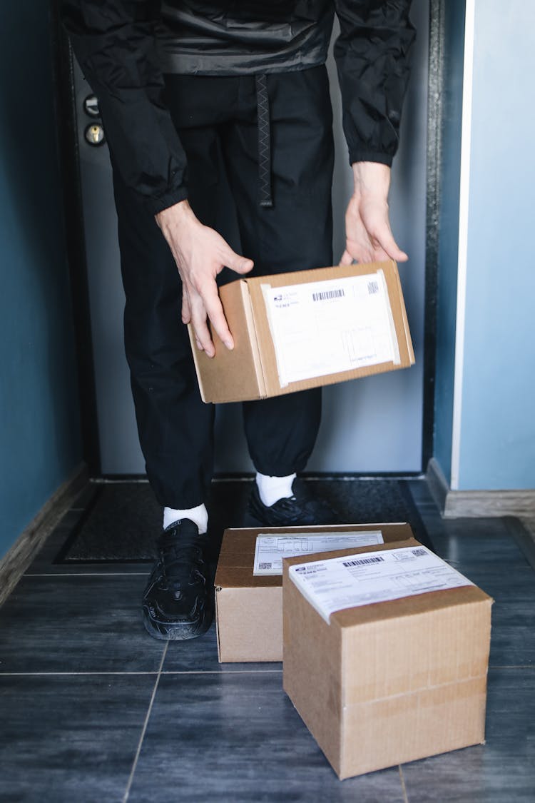 A  Person Standing On A Doorway Holding A Cardboard Box