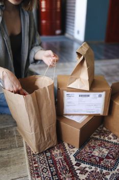Young woman unpacking paper bags and boxes from online shopping on a patterned rug at home.