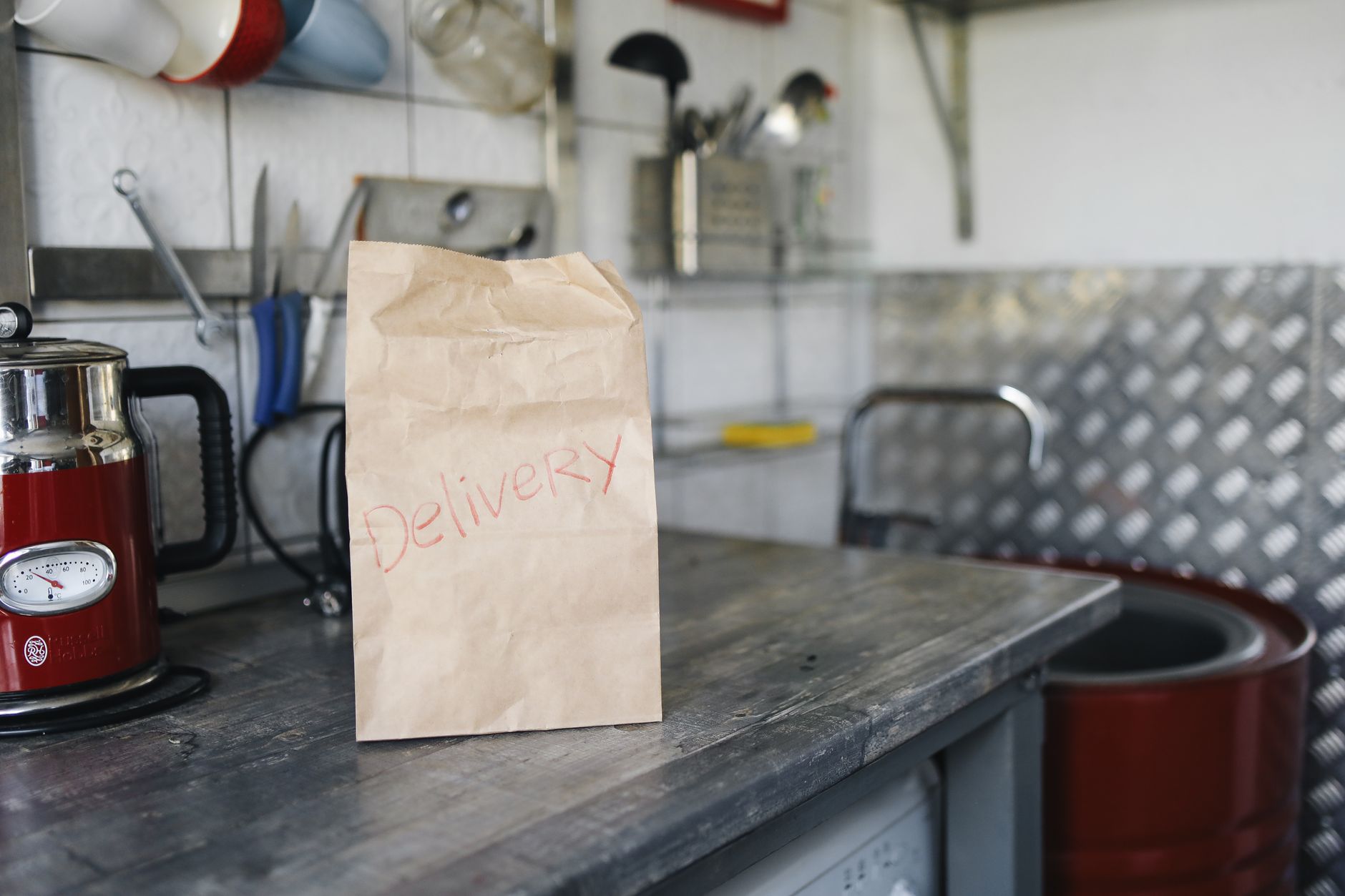 Paper bag labeled 'Delivery' on a metal kitchen counter with appliances.