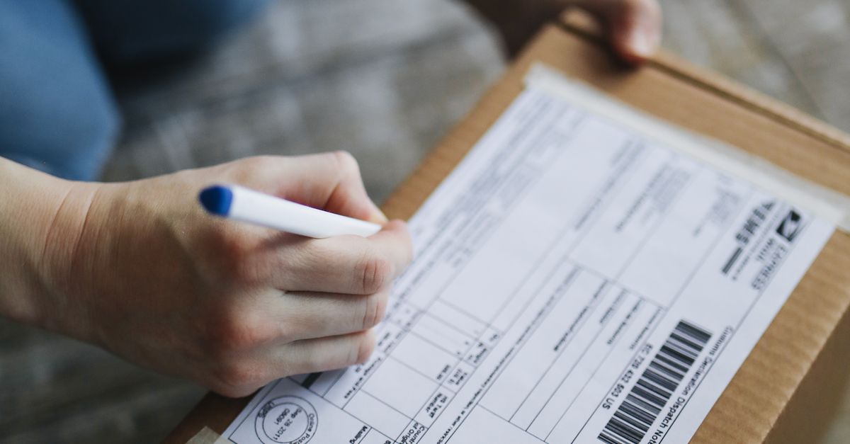 Hands writing delivery address details on a small cardboard shipping box, preparing a parcel for post