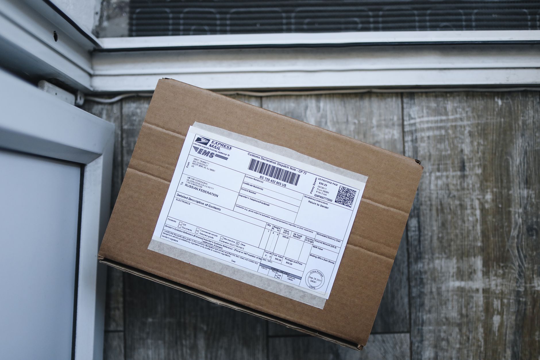Brown cardboard box with shipping label on wooden floor near door, ready for delivery.