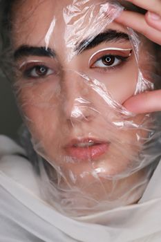 Confident female with bright makeup feeling choking and short of breath under cellophane