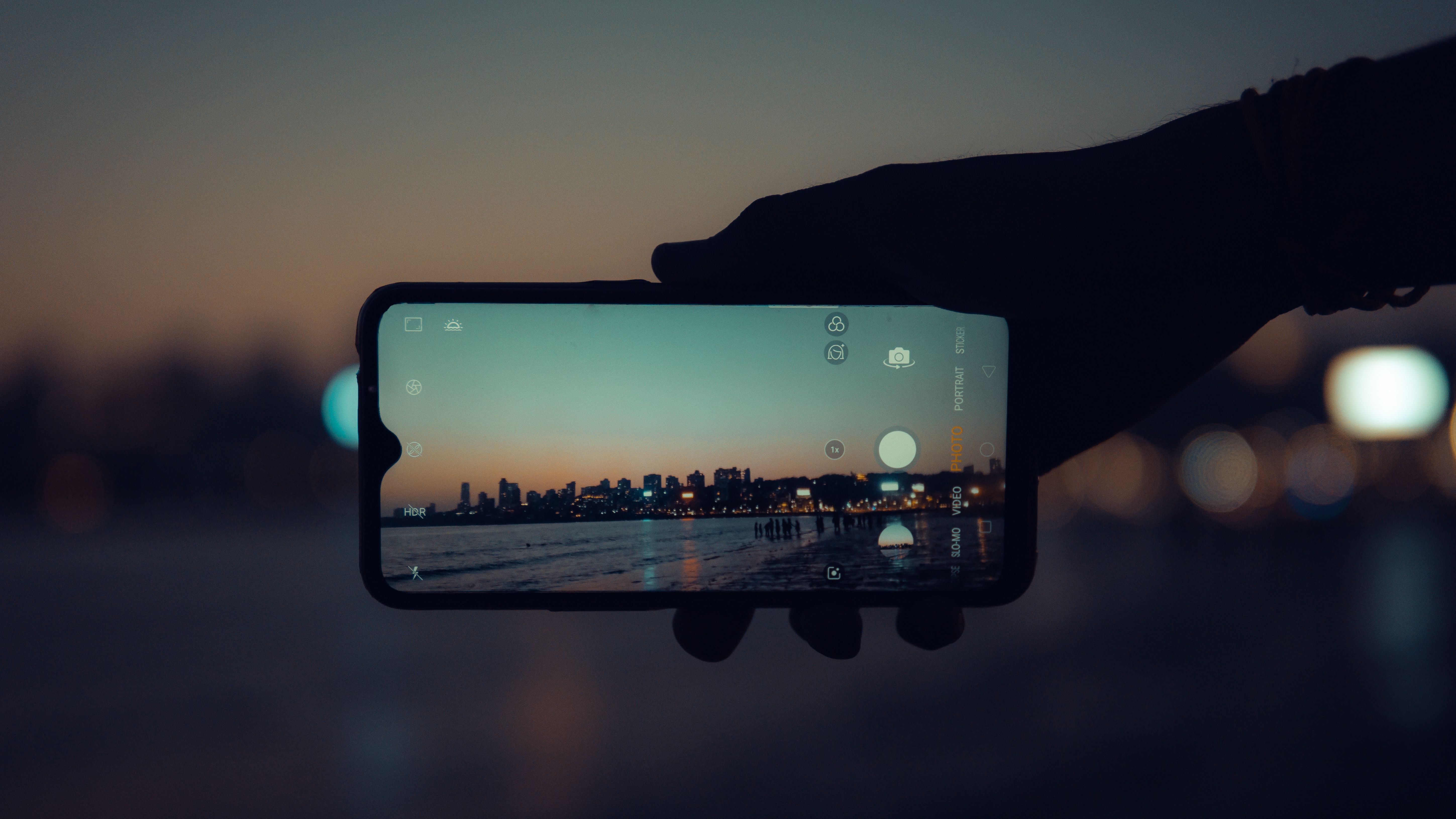 A smartphone capturing the Mumbai skyline at sunset with a clear reflection on its screen.