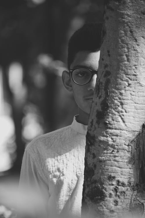 Ethnic man in eyeglasses behind tree trunk