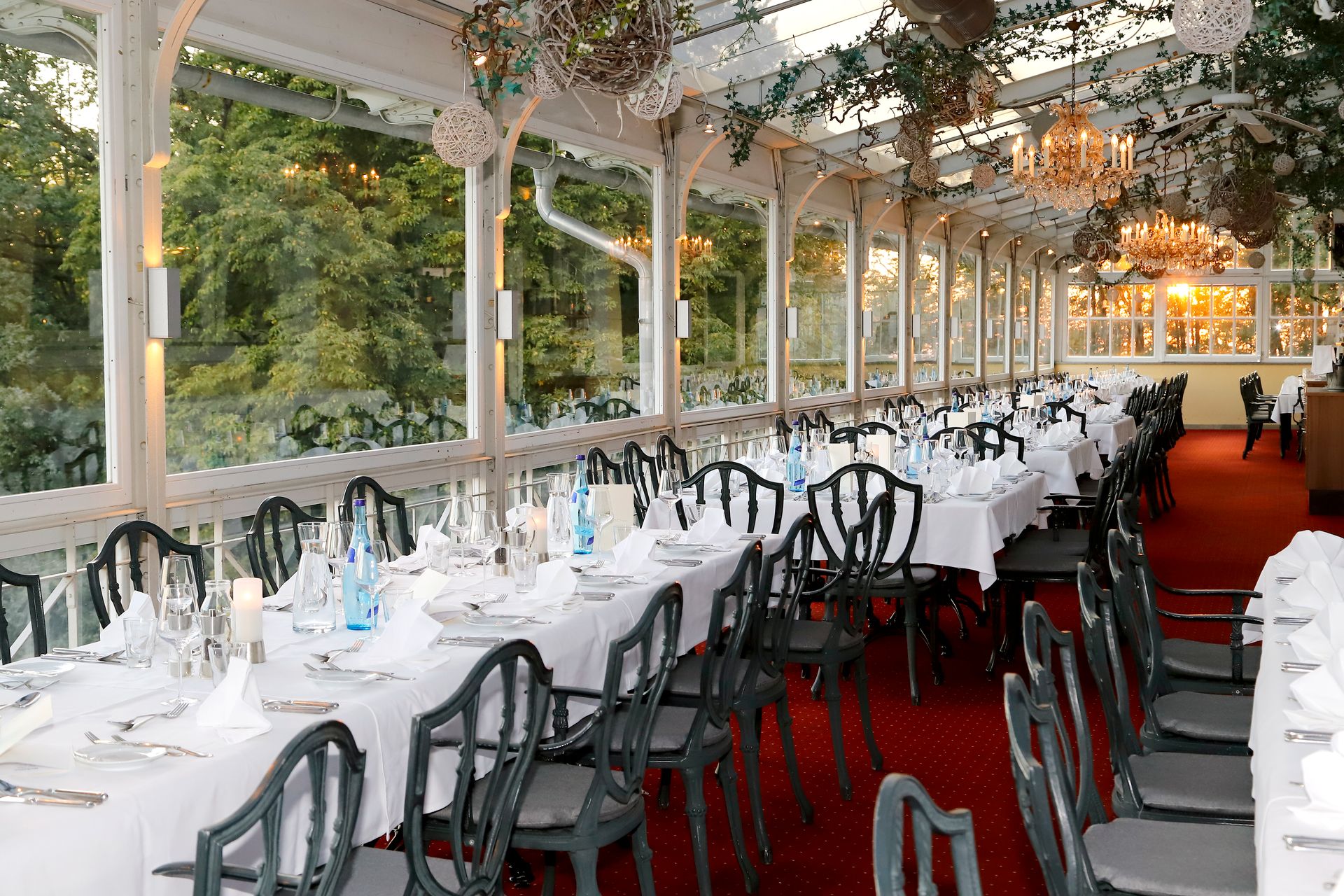 Elegant restaurant interior with formal place settings and chandeliers in a sunny conservatory.
