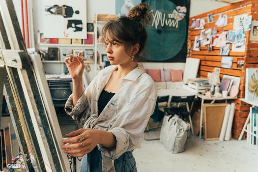 A focused young woman painting on a canvas in a creative art studio setting.
