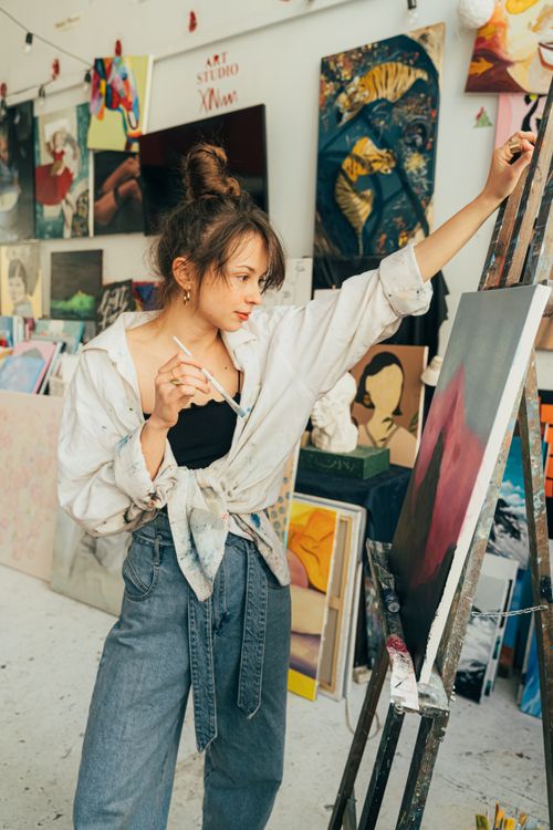 Free Artist passionately works on canvas in a vibrant art studio filled with diverse paintings. Stock Photo