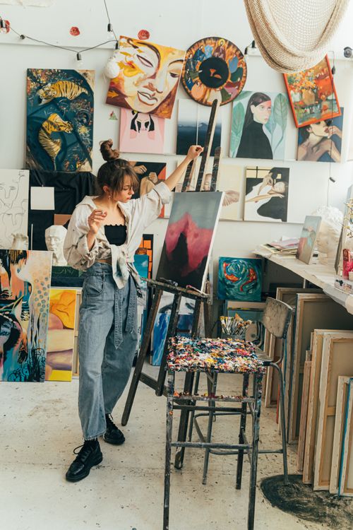 Free A creative young artist works on a painting in a studio filled with vibrant artworks. Stock Photo