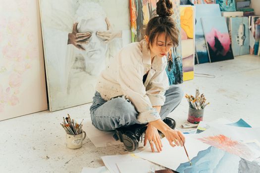 A creative young artist painting in a bright studio surrounded by artwork and brushes.