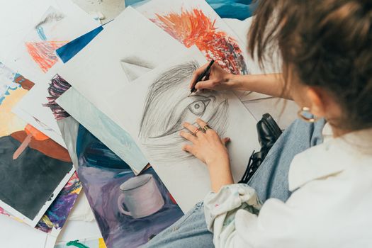 Artist sketching on paper surrounded by artworks, capturing creativity in an art studio.