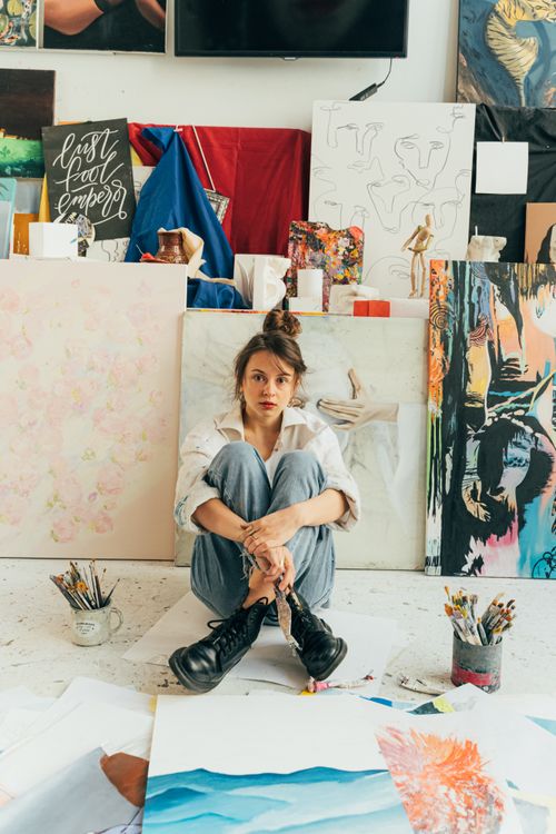 Free A young female artist sits pensively amidst her colorful artworks in a vibrant studio space. Stock Photo