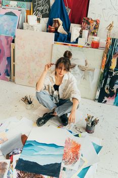 在明亮的工作室里，一位女艺术家坐在色彩缤纷的画作和艺术用品中间