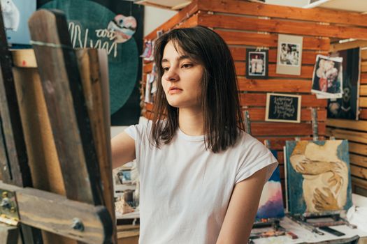 A young woman focused on painting in her art studio, surrounded by creative work.