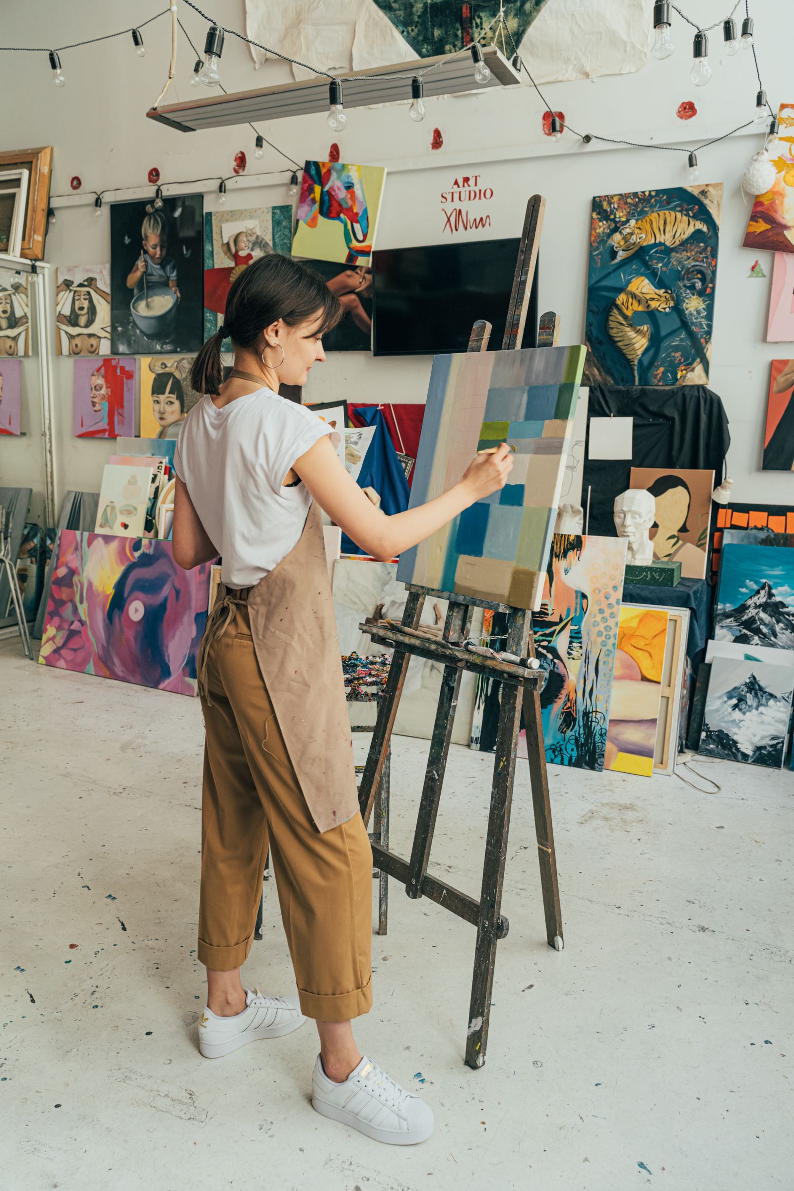Painter building a geometric composition at an easel in a busy studio