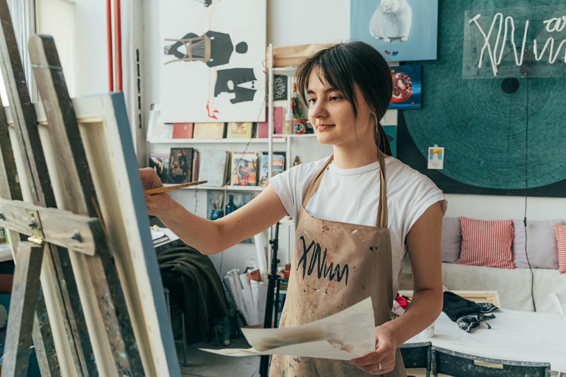 A young female artist focused on painting in an indoor studio setting.