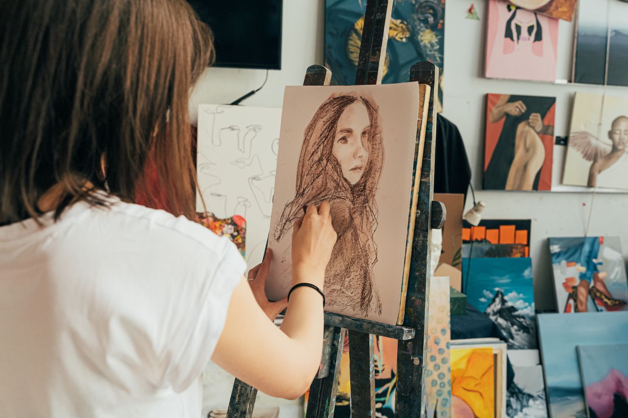 woman drawing in an art studio surrounded by finished paintings and ar