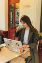 一位穿着外套的女人在户外咖啡馆里，一边喝咖啡一边用笔记本电脑工作