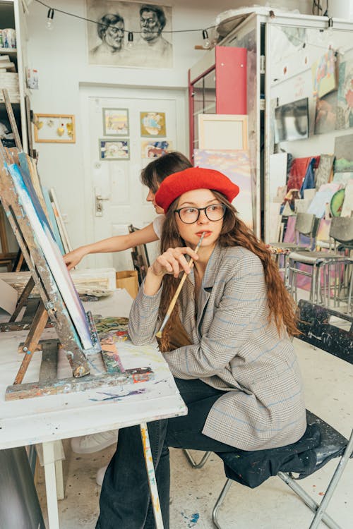 Woman in Gray and White Striped Long Sleeve Shirt Wearing Red Hat Sitting on Chair