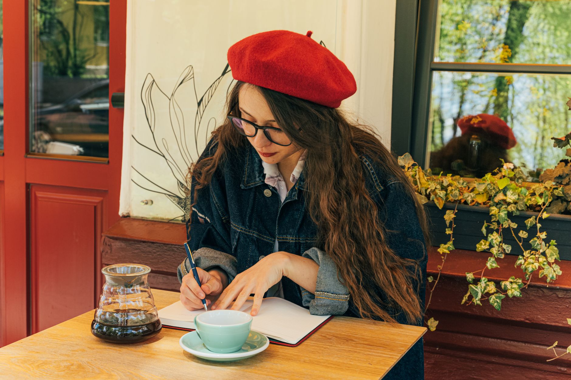 Woman in red beret writing in a café, sipping coffee, and enjoying a peaceful moment.