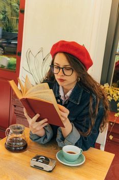 一位戴着贝雷帽和眼镜的女人在咖啡馆里看书，桌上放着一杯咖啡