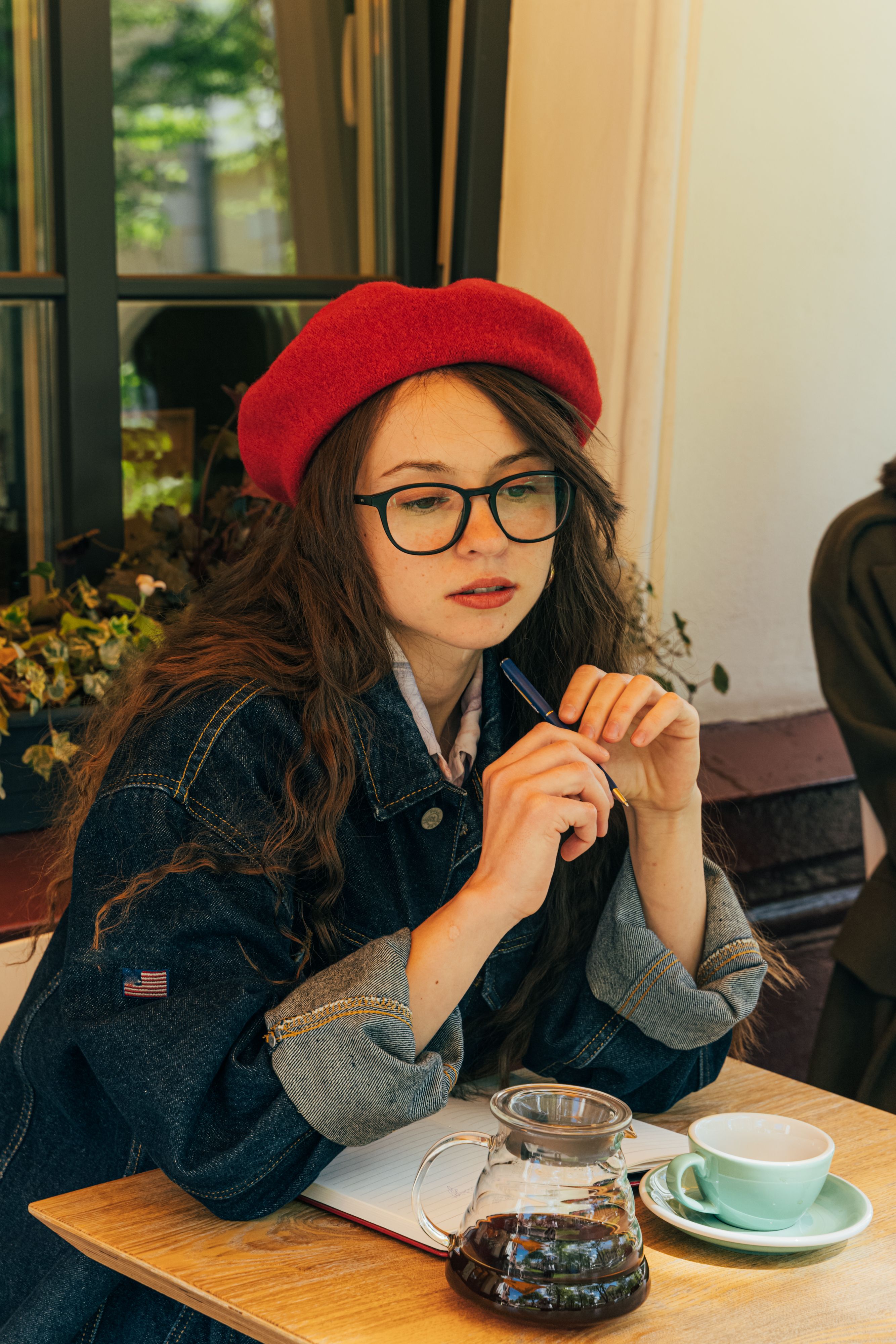 咖啡馆里，一名戴着眼镜、穿着牛仔夹克的女子正在喝咖啡