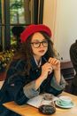 咖啡馆里，一名戴着眼镜、穿着牛仔夹克的女子正在喝咖啡