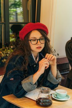 咖啡馆里，一名戴着眼镜、穿着牛仔夹克的女子正在喝咖啡
